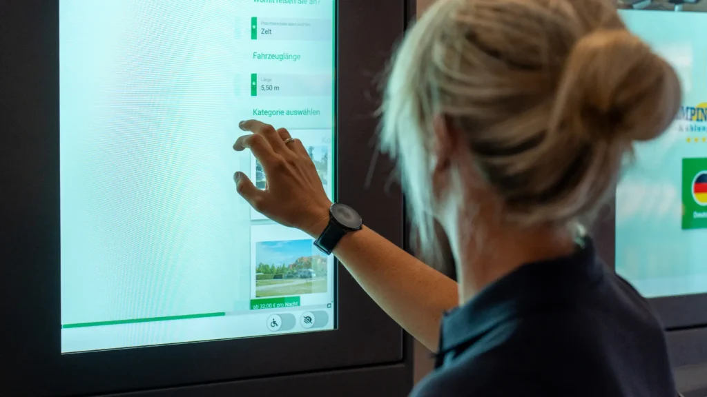 Campingplatz-Mitarbeiterin-bedient-Self-Service-Buchungsterminal-an-der-Rezeption